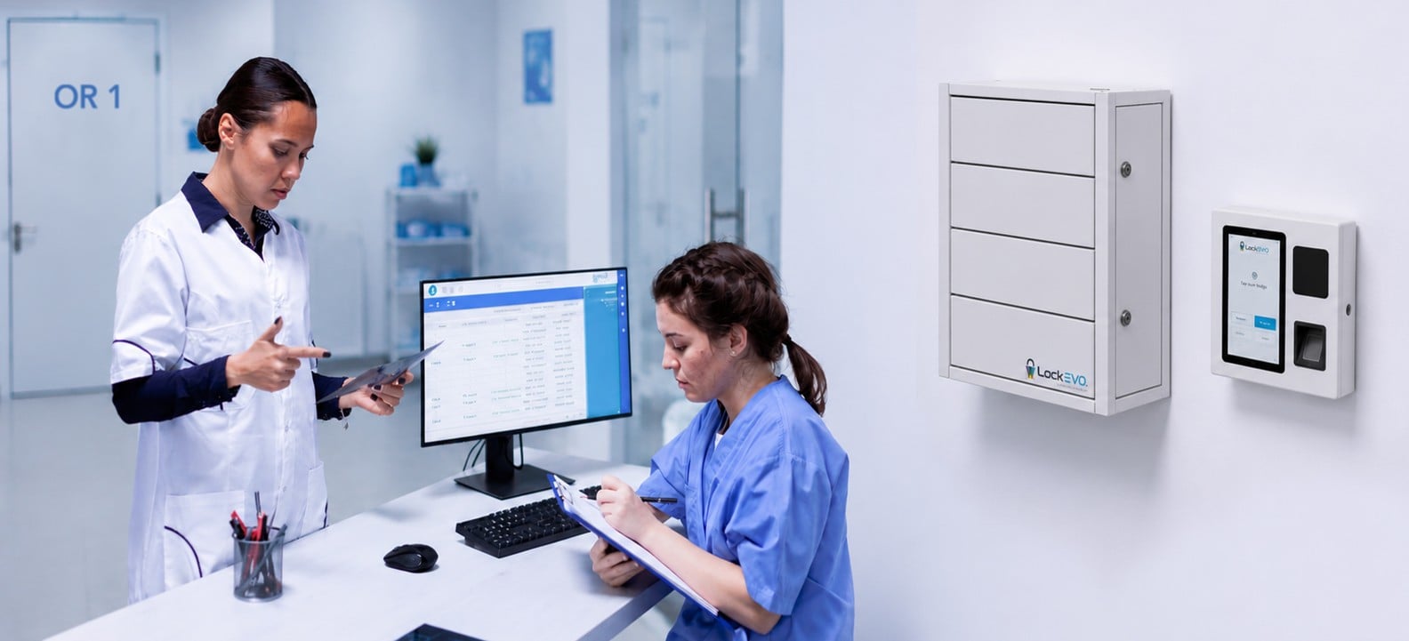 Clinical staff reviewing inventory on a monitor next to a wall-mounted Lockevo cabinet and CommandHub in an ASC hallway